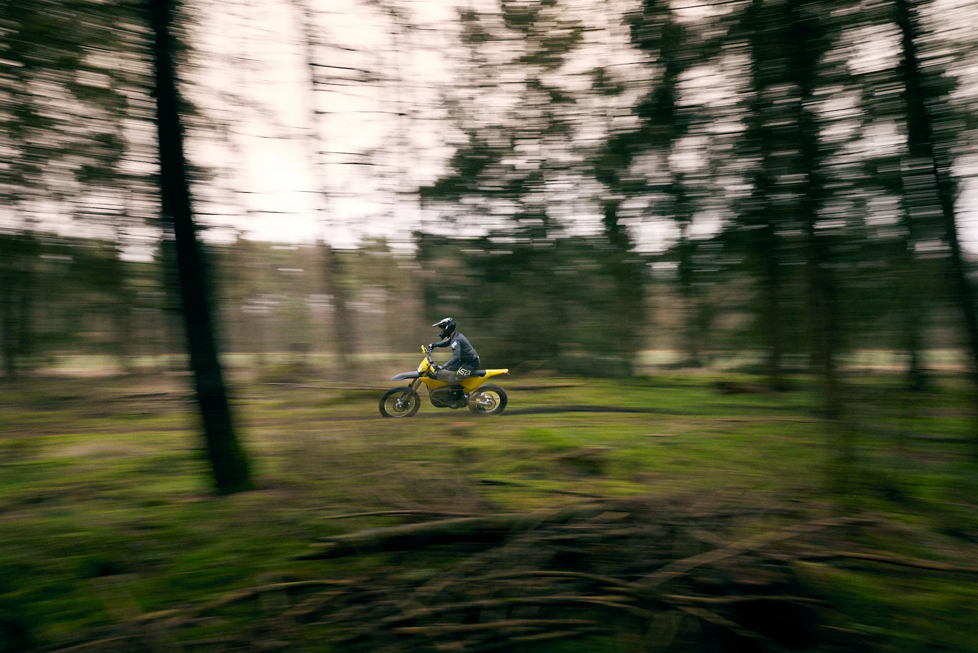 Person riding a yellow dirt bike at speed through a blurred forested area.