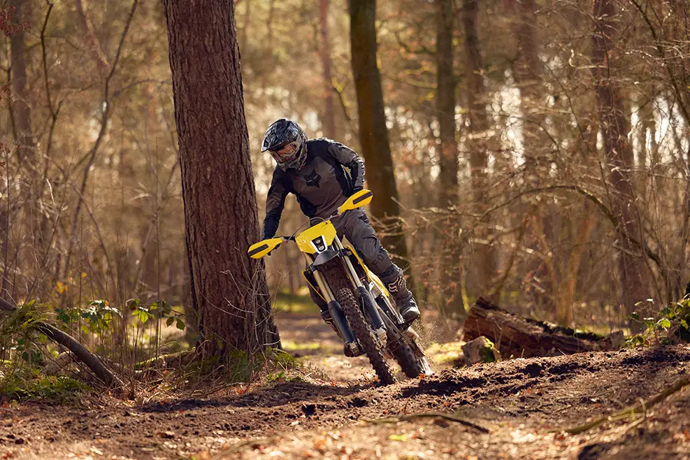 Person riding a yellow dirt bike through a forest trail wearing a helmet and protective gear.