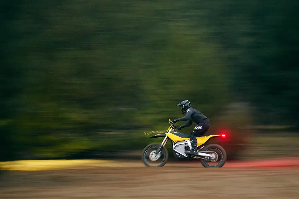 Person riding a yellow dirt bike quickly on a trail with blurred background of green trees.