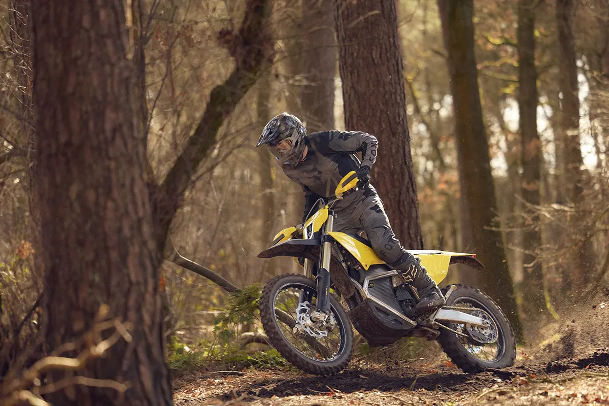 Person wearing protective gear riding a yellow dirt bike through a forest trail.