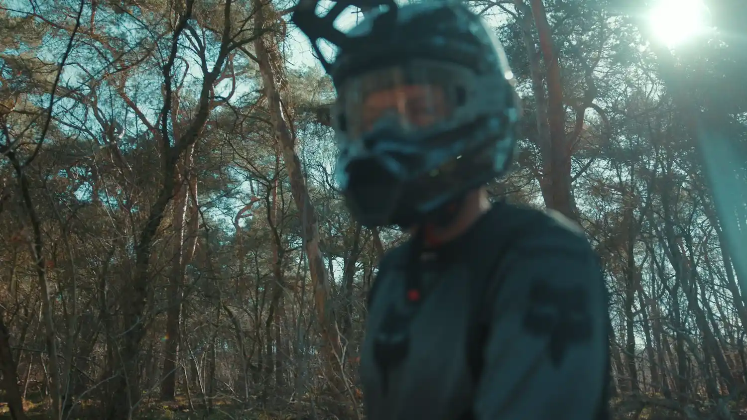 Person wearing a black mountain biking helmet and gear standing in a sunlit forest.